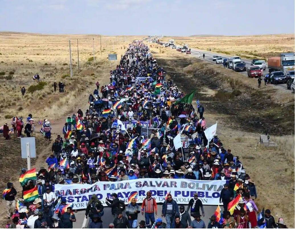 Fotografia aérea de uma passeata com milhares de trabalhadores bolivianos em uma rodovia de uma zona rural da Bolívia.