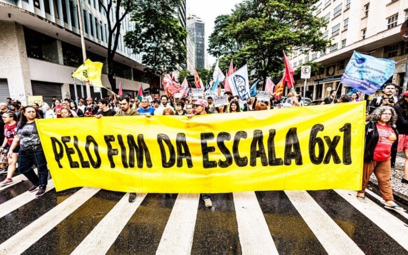 Fotografia de manifestantes em Belo Horizonte. À frente, uma faixa amarela com as letras pretas: "Pelo fim da escala 6x1".